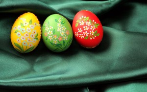 Three Easter eggs (red, yellow and green) lying on dark green satin fabric - textile.